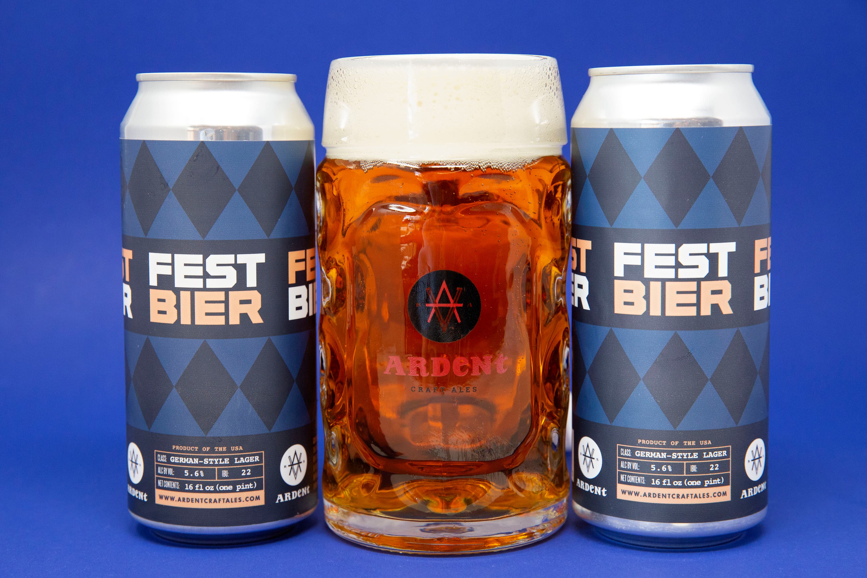 Blue cans of Festbier beside a stein of copper-colored beer on a blue background