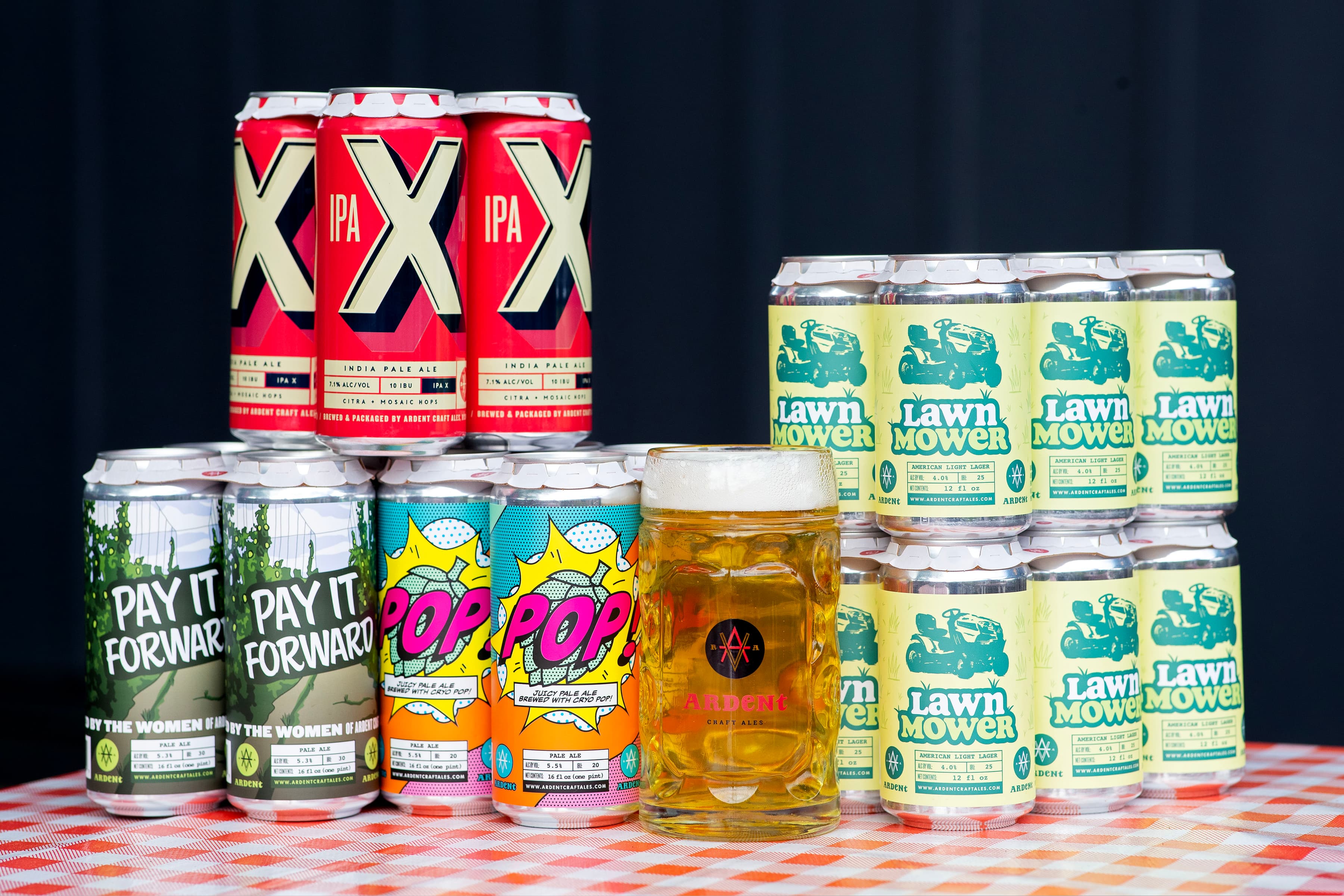 Various 4-packs and 6-packs of cans stacked behind a stein glass full of clear golden beer