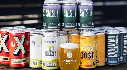 Many cans in different colors and sizes in front of a single stemless 12oz glass of beer