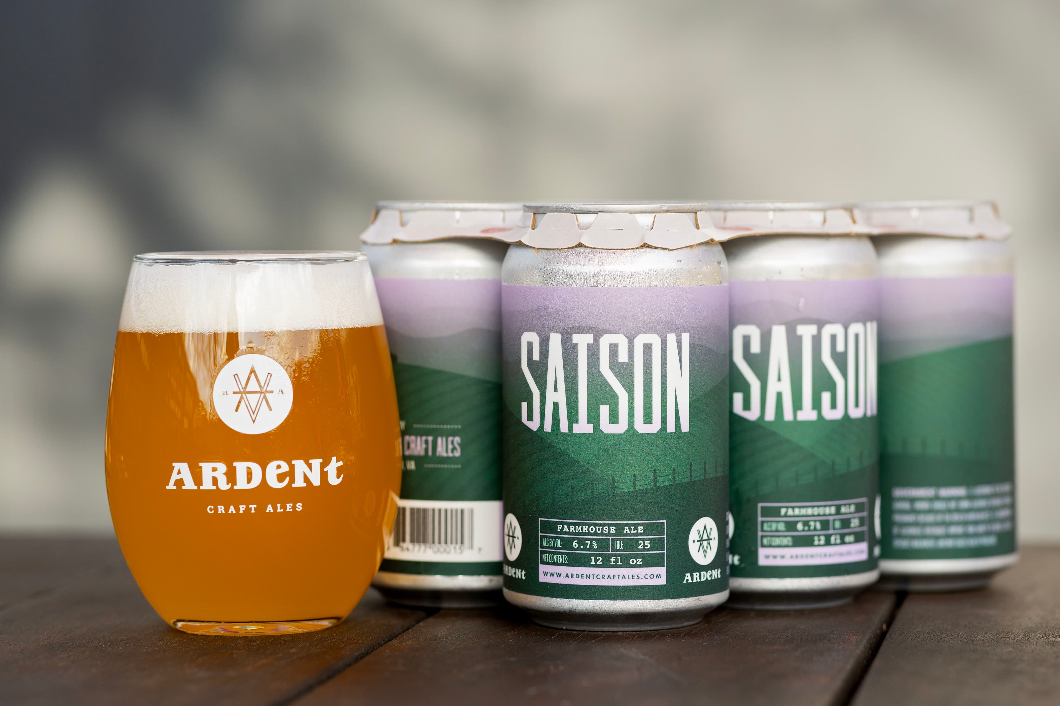 6-pack of 12oz green Saison cans with a stemless 12oz glass of cloudy golden beer
