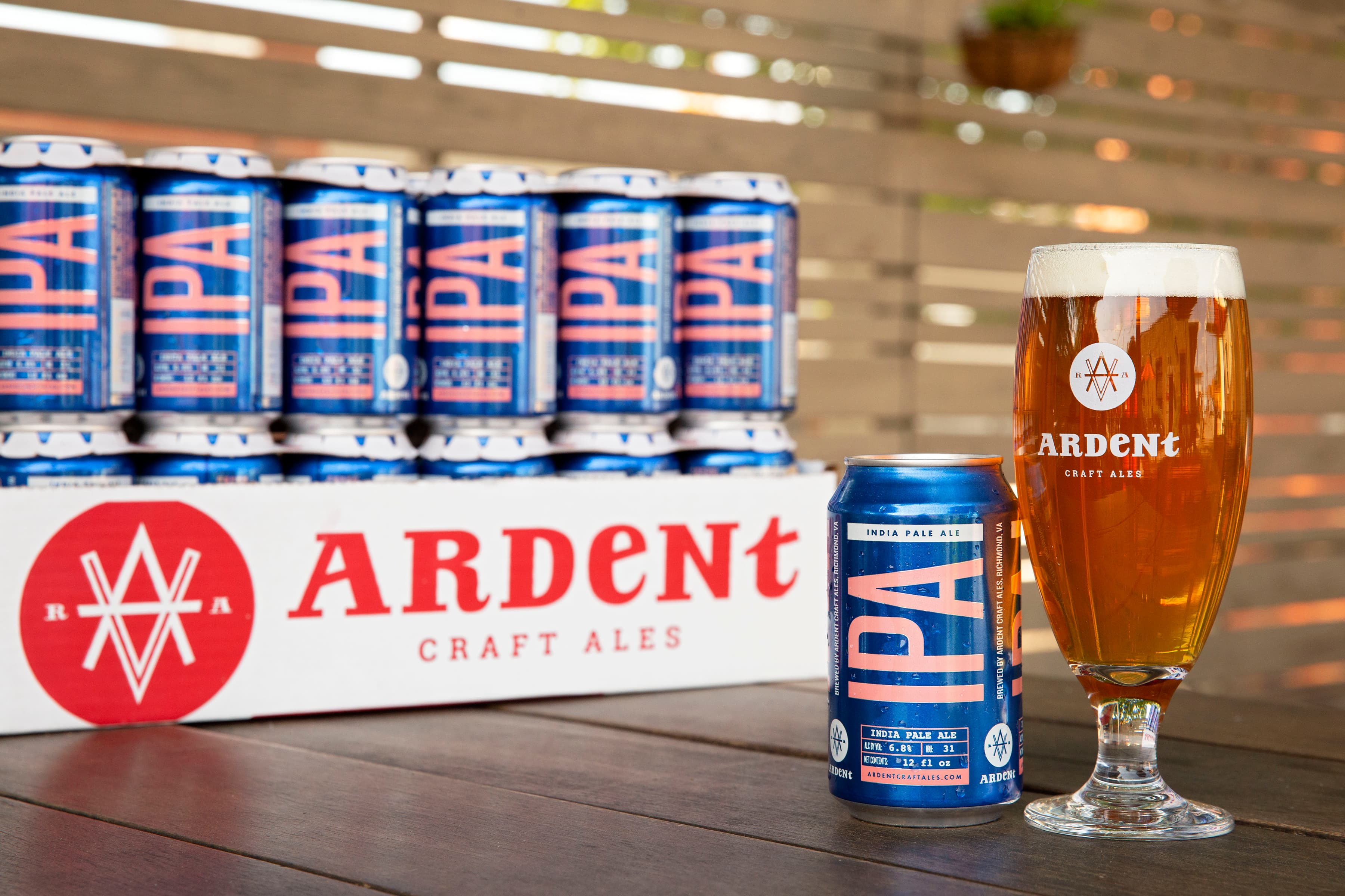 6-pack of blue 12oz cans of IPA with a 12oz stemeless glass of copper-colored west coast IPA over a white background
