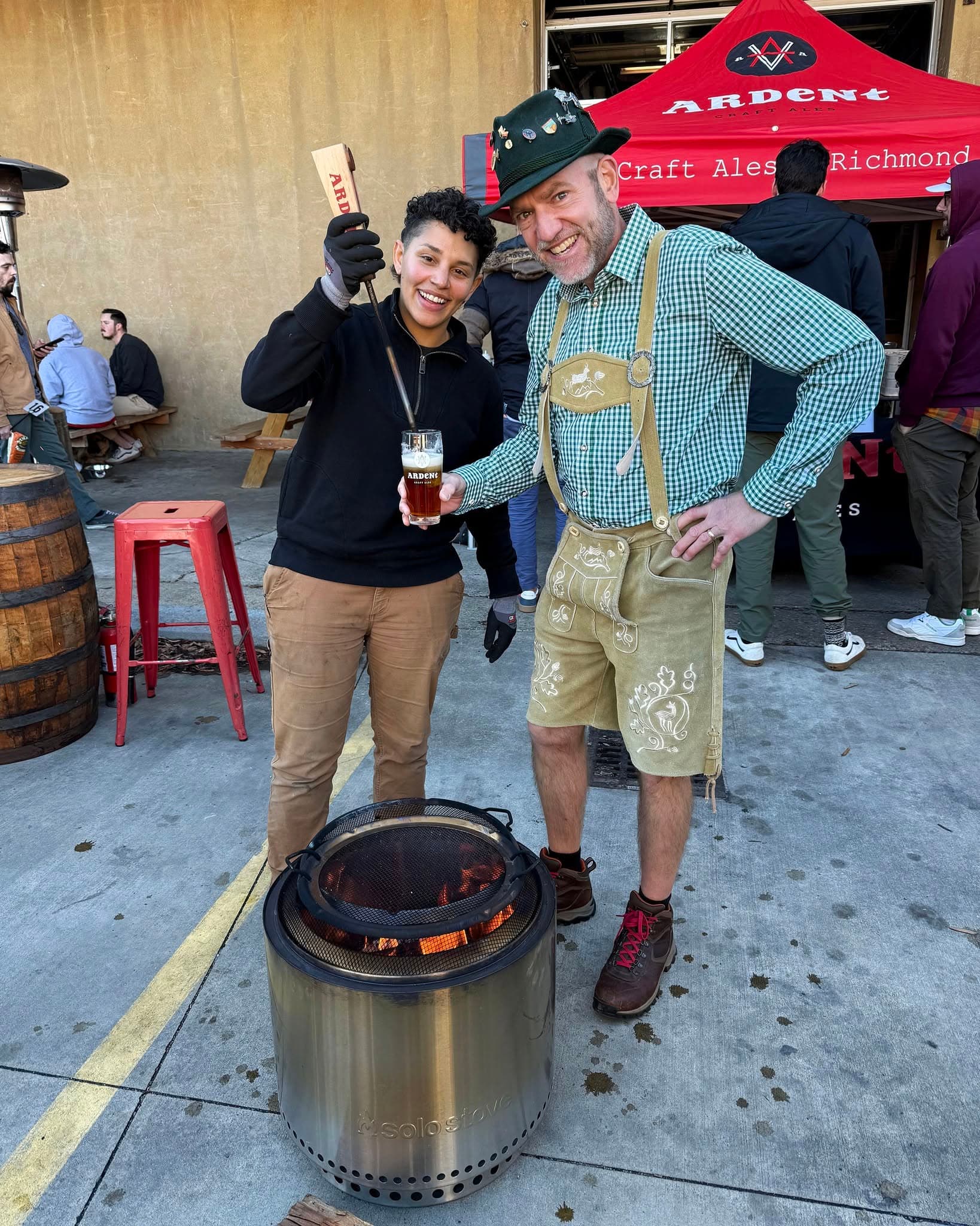 Two people standing in front of a fire pit while spiking a glass of beer with a hot rod