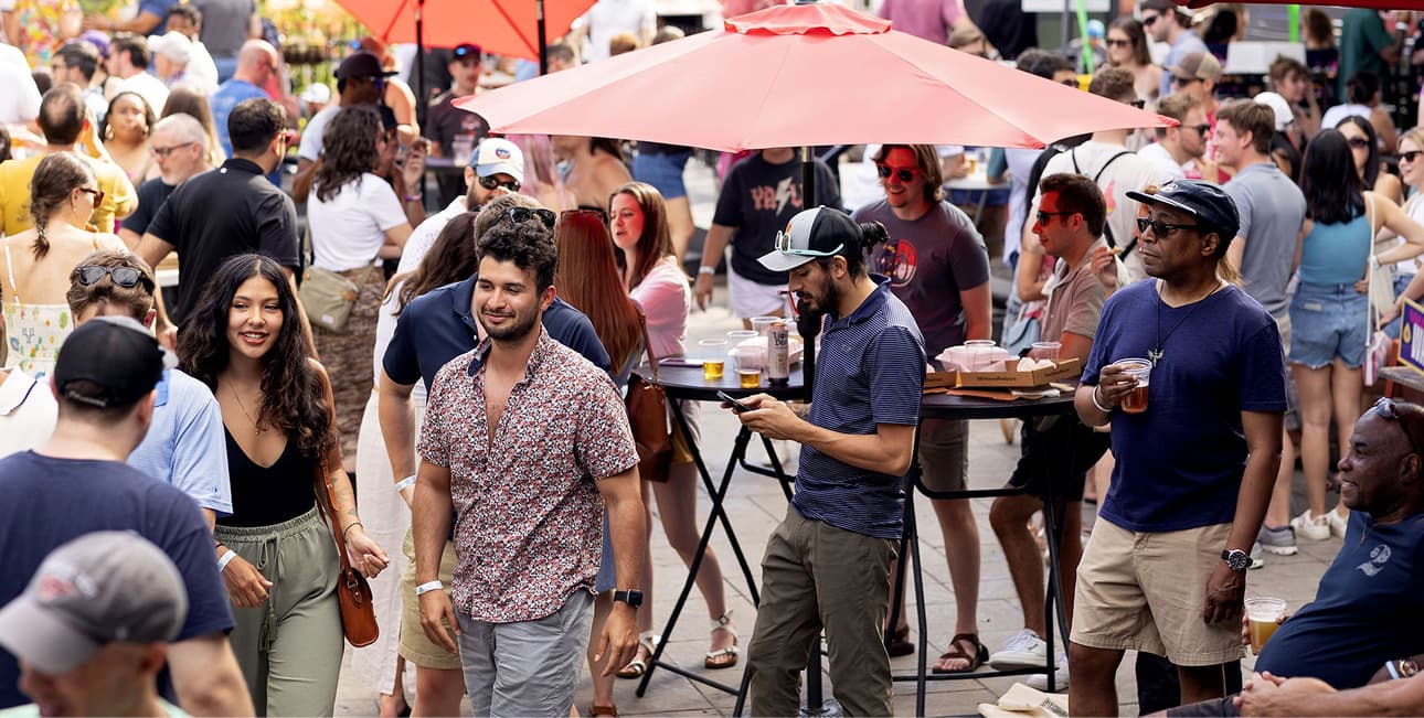 Crowds of people smiling outside around red umbrellas on a patio